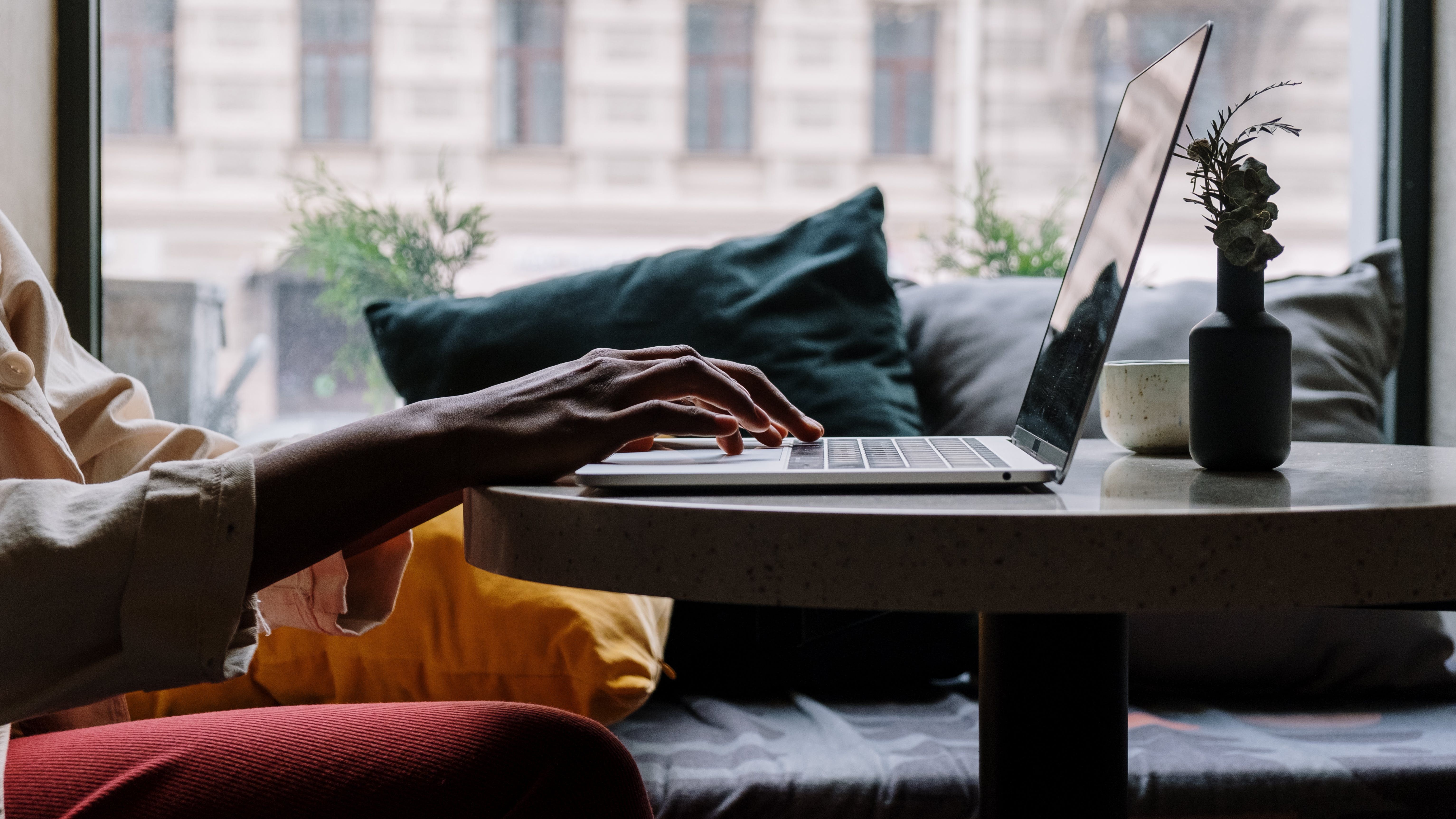 Woman out of frame sitting at a coffee table, working on a laptop completing a free online course.